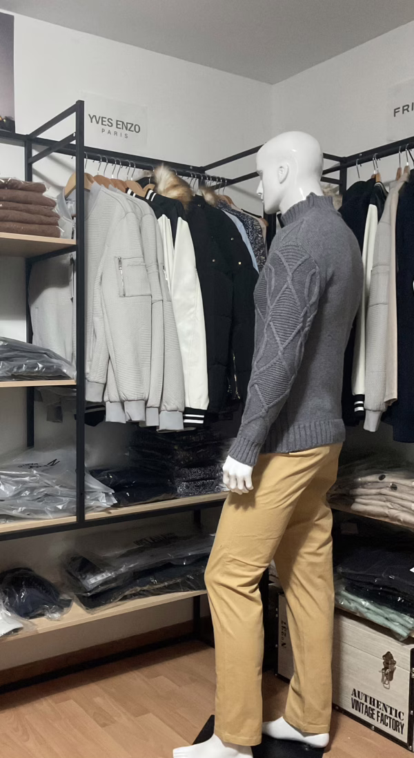 Photo prise de côté (photo complète) du pull torsadé au toucher cachemire gris de la marque Top Monday. On voit qu’il est associé avec le pantalon stretch beige sable de la marque Yves Enzo.