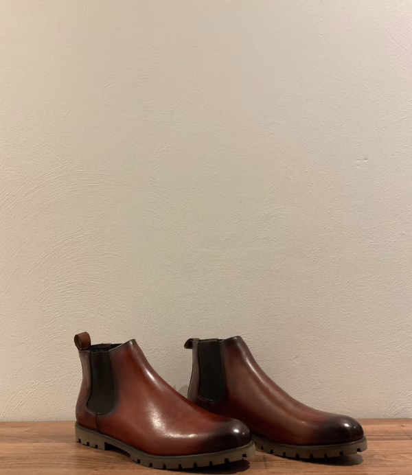 La photo de face présente les bottines Chelsea couleur cognac, un modèle intemporel qui allie élégance et caractère. Leur cuir lisse aux reflets chauds met en valeur un dégradé subtil vers le bout plus sombre, apportant du relief et de la profondeur au design. La semelle épaisse crantée assure à la fois style et robustesse.