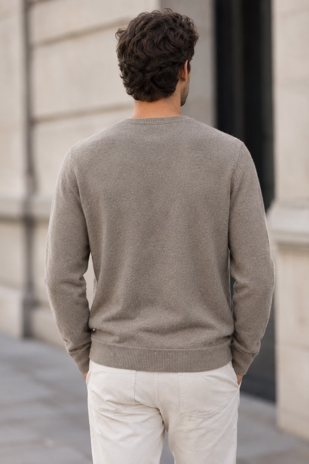 Vue de dos d'un homme portant le pull col V en cachemire taupe "five ever", posant en extérieur.