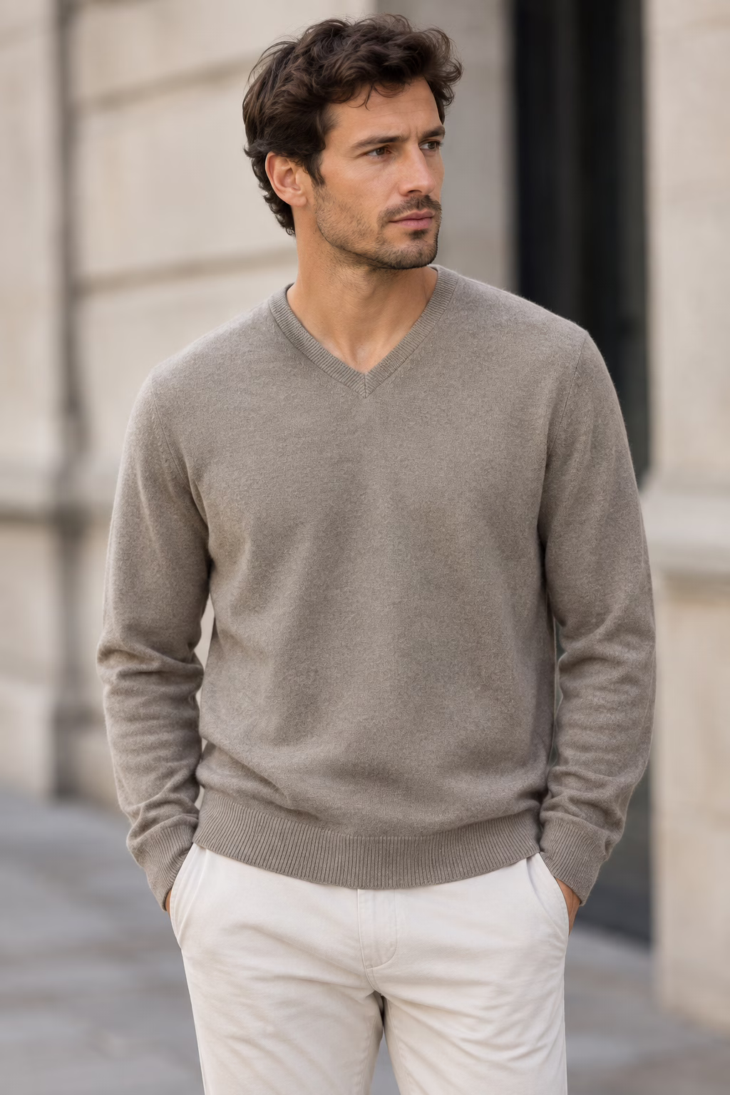 Homme portant un pull col V en cachemire taupe "five ever" et un pantalon écru, posant en extérieur.